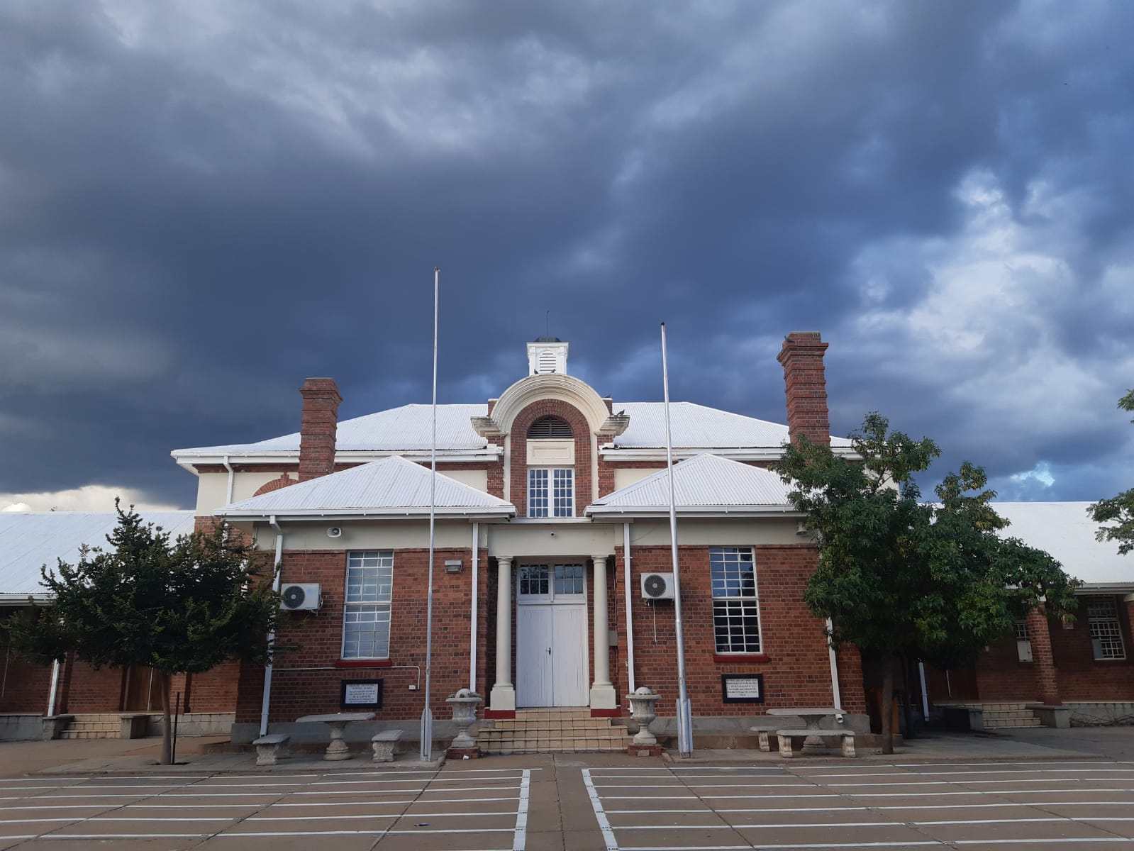 Front view of Vryburg High School main building under dark rain clouds in Vryburg, North West, South Africa.